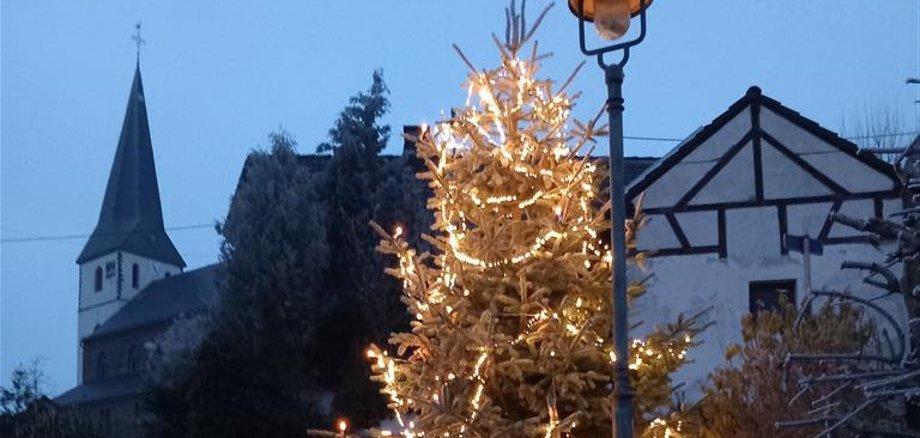 Weihnachtsbaum mit leuchtender Lichterkette im Hintergrund ist der Kirchturm